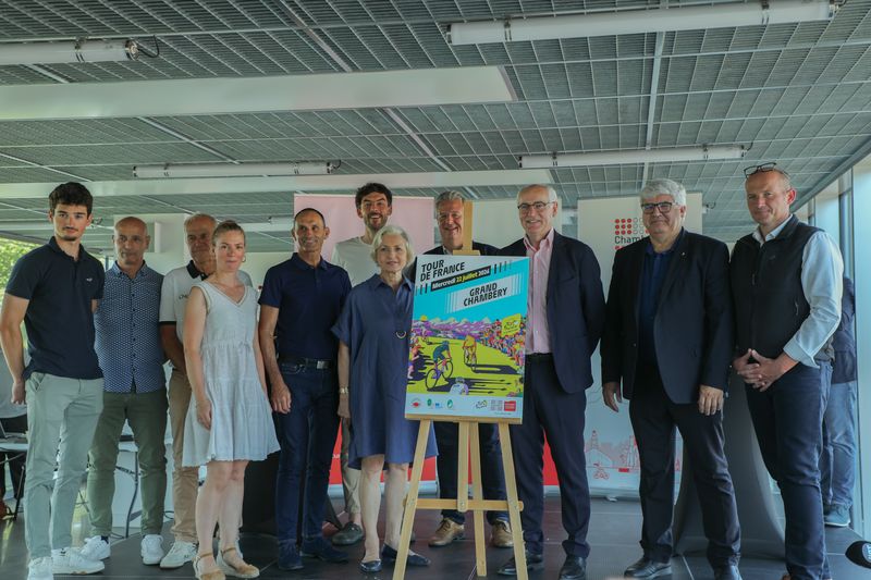 des hommes et femmes posent pour la photo autour de l'affiche du Tour de France 2026