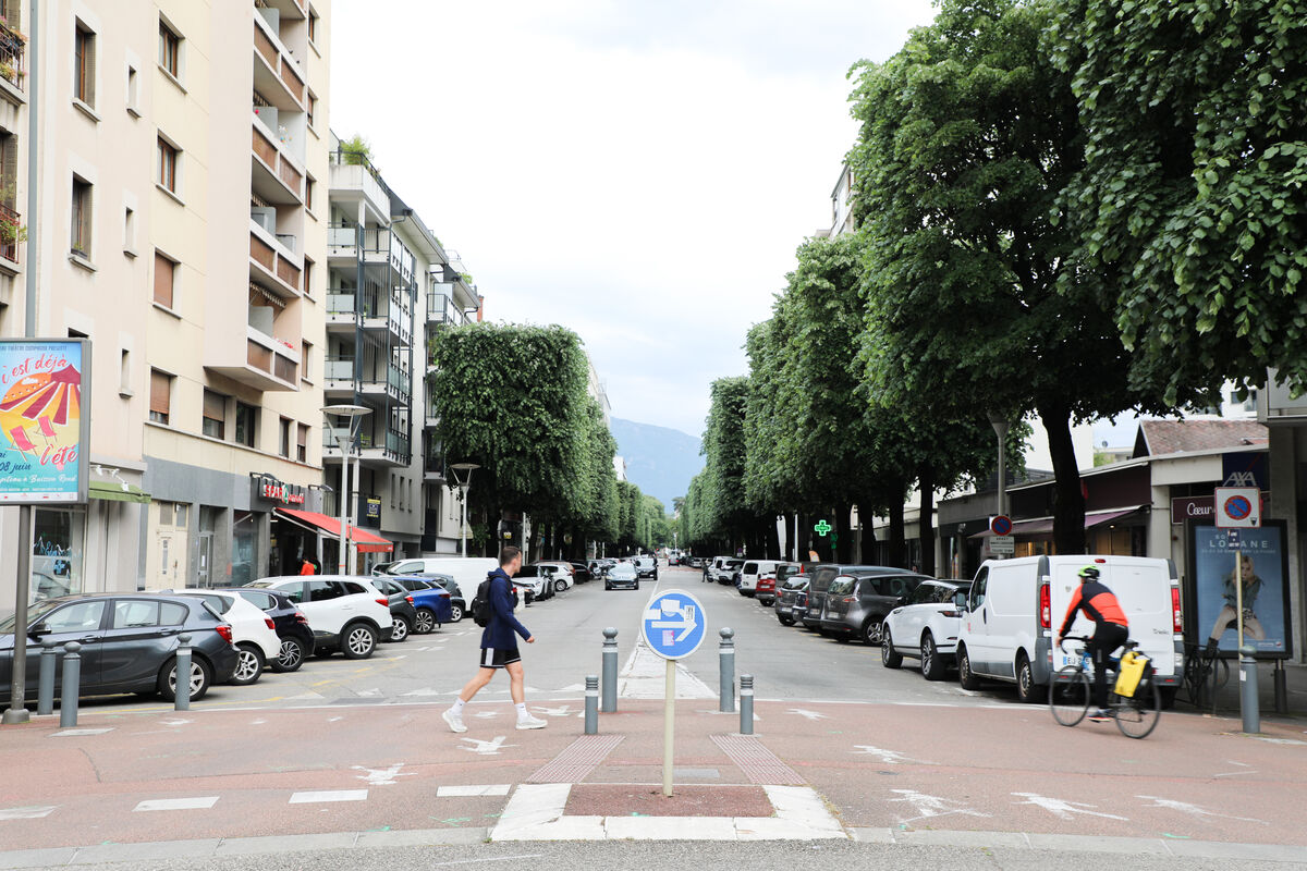 Vue sur une rue de Chambéry, un piéton traverse la route et un vélo circule sur la voie automobile